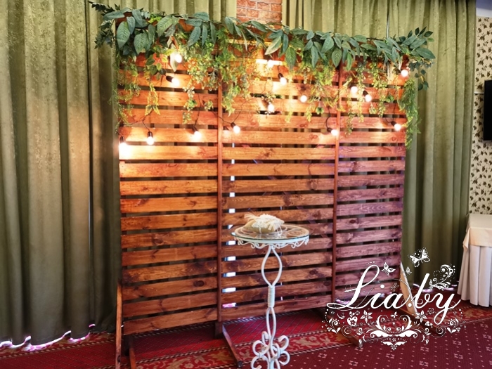 деревянный фон , ретро-гирляндой, белым столиком и зеленью на свадьбу в Дрозды клаб