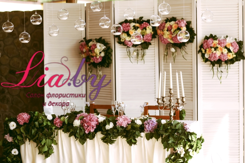 Интересное украшение стола для молодоженов на свадьбе с использованием цветов, свечей, тканей и подсвечников подвешенных над столом
