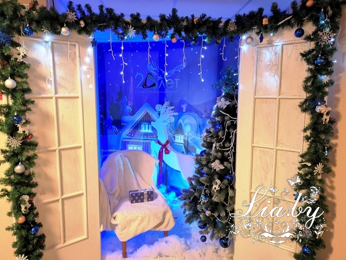 Фотозона в фойе финансового учреждения на Рождество Христово и Новый год. Выполнена как "дверь в зимнюю сказку" за которой открывается сюжет зимы на фоне печатного ПВХ баннера установлена украшенная ель, фигура оленя, кресло для гостя с белым пледом.