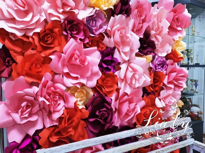 цветочная стена из цветов розового, красного и бордового цвета, а также белая деревянная кованная садовая лавка в качестве фотозоны на 8 марта в фойе