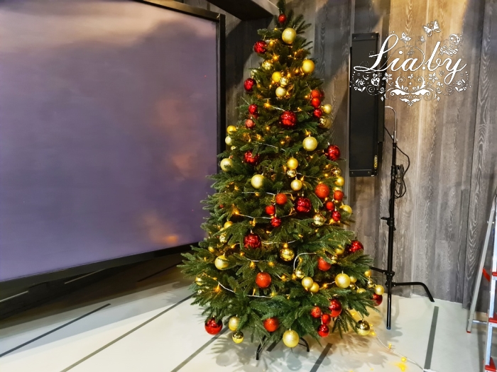 украшение телестудии к новому году: украшение стола ведущего новогодней елью с подарками, хвойная гирлянда, композиция из подарков с подсветкой