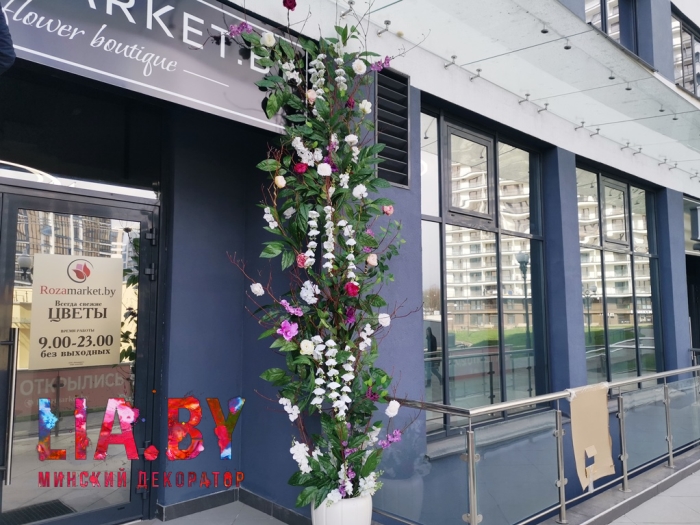 украшение входа в цветочный магазин композициями из искусственных цветов и зелени обрамляющих вход в вазах