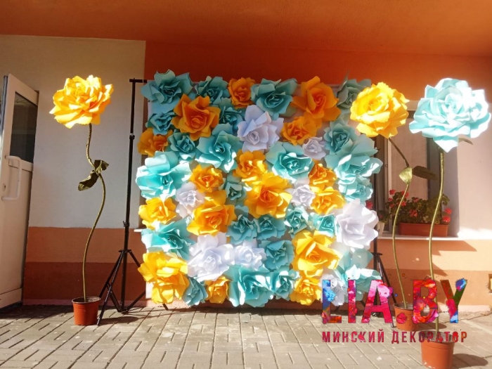 Фотозона стена из желтых и бирюзовых бумажных цветов с ростовыми цветами гигантами