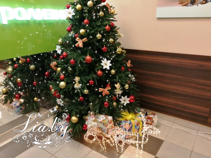 Украшение вестибюля офиса новогодней елью с подарками и светящимся оленем с санями