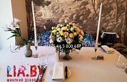 украшение столика в ресторане пышной цветочной композицией из натуральной розы, эустомы и зелени в белых и нежно желтых тонах, подсвечниками с высокими белыми свечами
